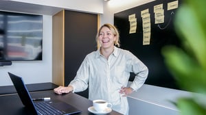 Stine står smilende ved et bord foran en tavle med gule lapper.